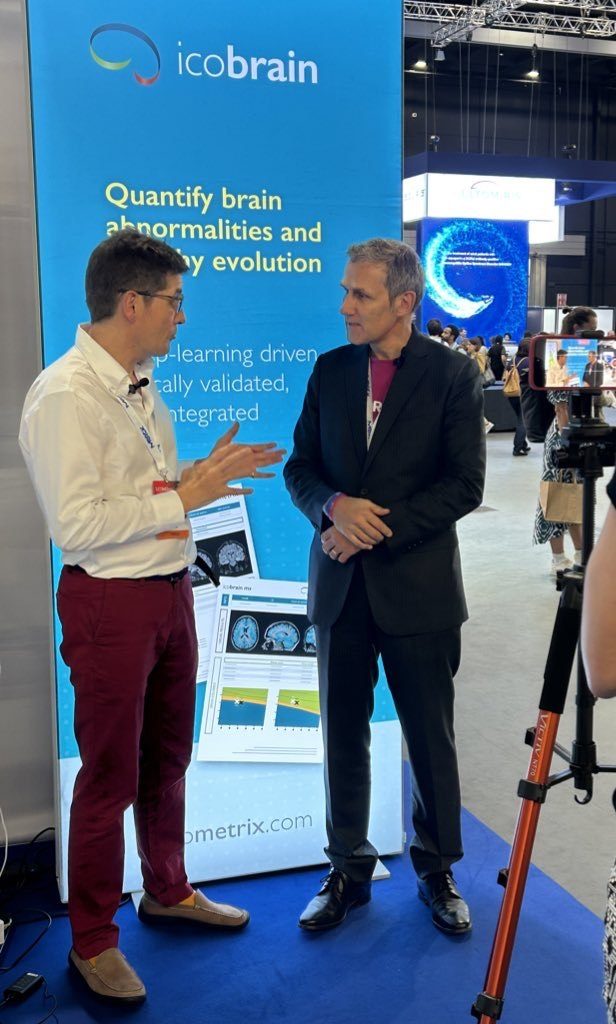 Dominic in conversation with Professor Klaus Schmierer in front of an icobrain display at a congress stand